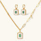 Gold-plated jewelry set with white enamel square pendants and emerald CZ stones on cream background.