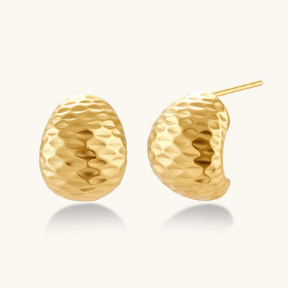 Pair of textured gold-plated sterling silver huggie earrings with dimpled surface finish on cream background.