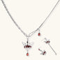 Silver-tone crown pendant with red zirconia stones and matching asymmetrical earrings on cream background