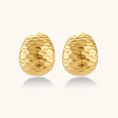 Pair of textured gold-plated sterling silver huggie earrings with dimpled surface finish on cream background.