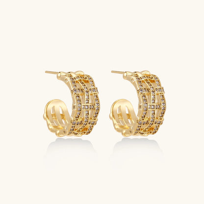 Gold-plated geometric hoop earrings with basket-weave lattice design and pavé crystal accents on cream background
