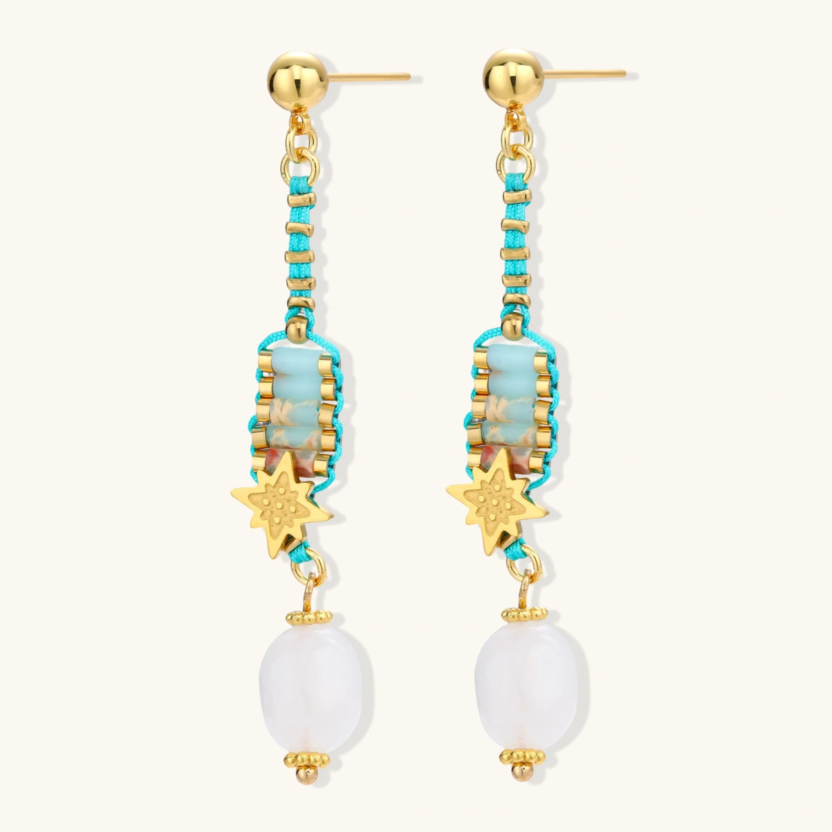 Gold-plated dangle earrings with turquoise threading, star charms, and white pearl beads against cream background.