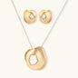 Close-up of organic gold-toned earrings and necklace with white baroque pearls on neutral background.