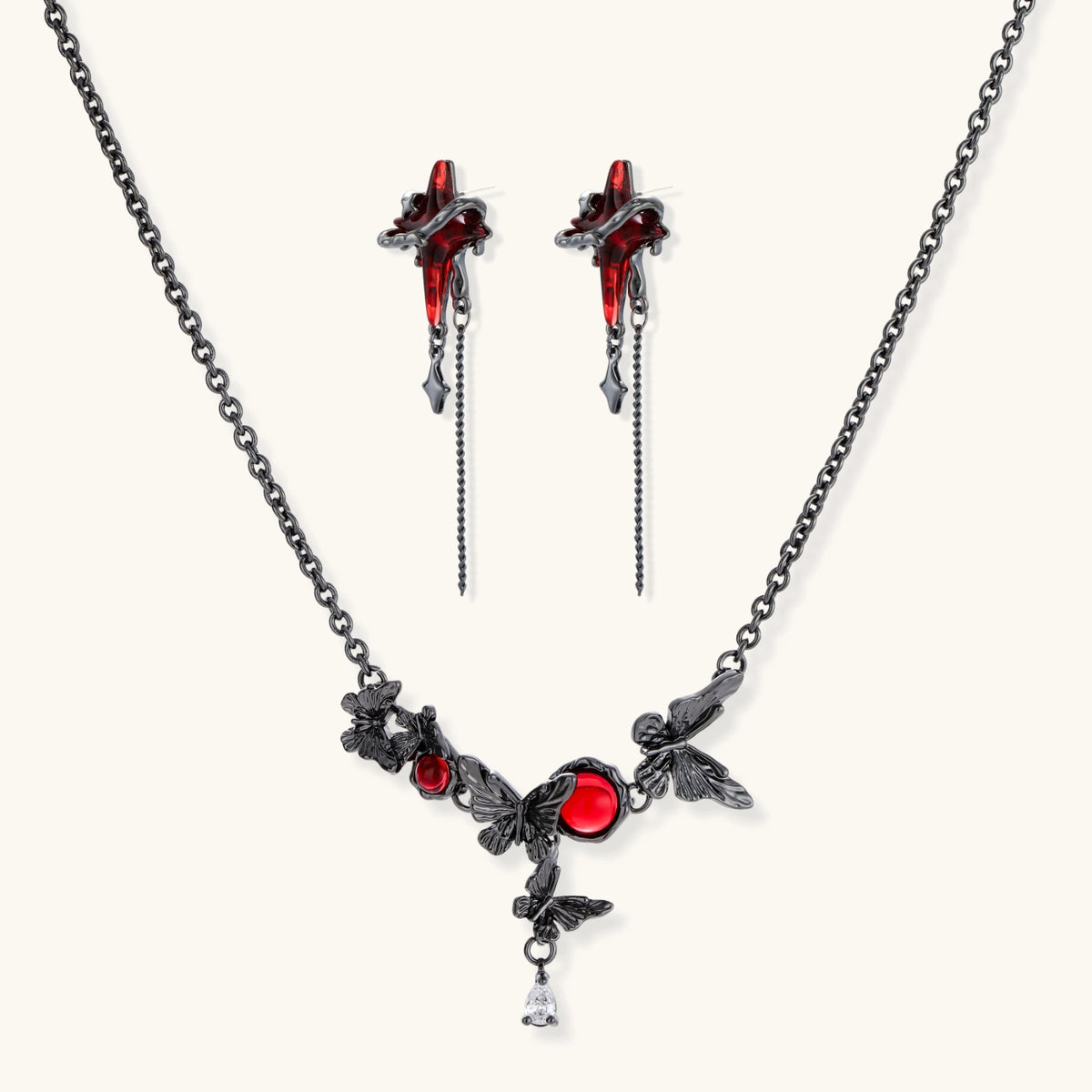 Gothic jewelry set with red resin cross pendants wrapped in dark metal chains on cream background.