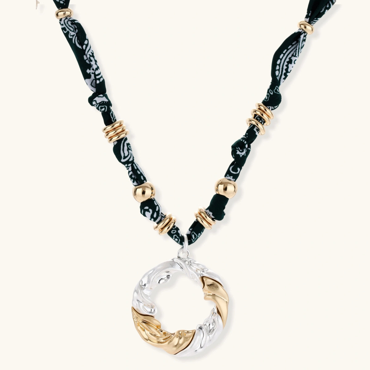 Adjustable necklace with black paisley fabric cord, gold metal spacers, and clear twisted pendant on cream background