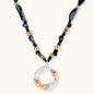 Adjustable necklace with black paisley fabric cord, gold metal spacers, and clear twisted pendant on cream background