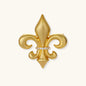 Ornate gold-plated fleur-de-lis brooch with crystal band detail on white background, showing brushed metal finish.
